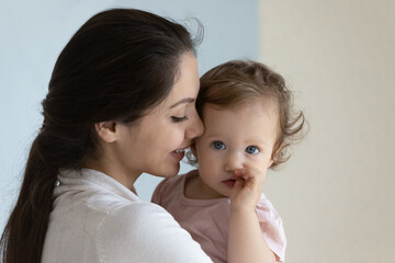 Happy beautiful new mom holding cute toddler baby in arms, smiling, kissing little kid with love, tenderness. Mother hugging, cuddling infant child, enjoying maternity leave after childbirth. Close up