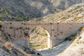 Fototapeta premium Small brick and masonry bridge over a dry riverbed surrounded by mountains. Drought concept. 