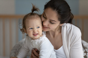 Happy sweet new mom cuddling cute baby, hugging, kissing little daughter girl. Young mother holding smiling toddler in arms with love, care, tenderness, enjoying motherhood, bonding with kid