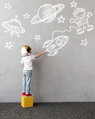 Happy kid draws a chalk rocket on the wall