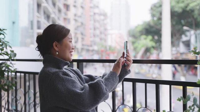 one happy young asian woman traveling in the city using mobile phone video call chatting online with friend on the urban balcony