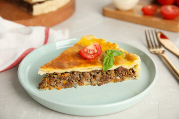 Piece of delicious pie with minced meat, tomato and basil served on light marble table, closeup