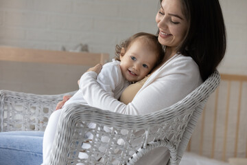 Smiling young mom hugging and cuddling little baby daughter with love and tenderness, enjoying...