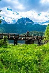 Tourist man on wooden footbridge over stream and Glacial Black Lake. Durmitor National Park. Montenegro.