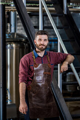 Young male brewer in leather apron at modern brewery factory