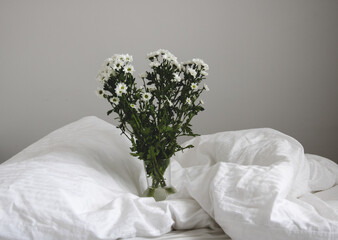 bouquet of white flowers in bed bedroom with  natural bed sheets blanket 
crumpled