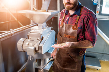 Obraz premium A young brewer in a leather apron controls the grinding of malt seeds in a mill at a modern brewery
