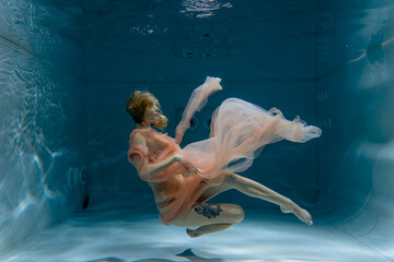 A girl with long dark hair swims underwater in a pink dress and with a crown on her head, like an underwater queen. Fairy tale suitable for advertising