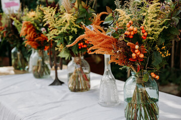 Rustic style. Boho style bouquets on the table in glass vases and jars. Wooden table and white...