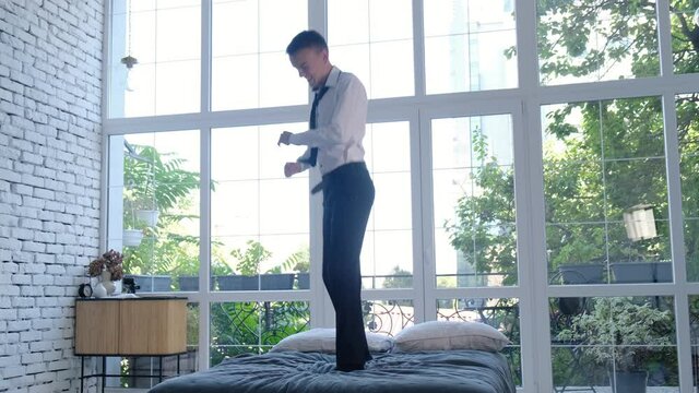 Satisfied man in business clothes jumping with happiness on the bed at home
