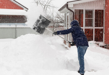 man in winter clothes shoveling snow during snowstorm in backyard. Winter weather. shallow depth of...