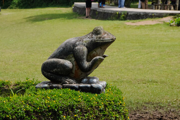 stone statue of a frog in a park on a flowerbed.