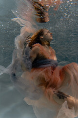 A girl with long dark hair swims underwater in a pink dress and with a crown on her head, like an underwater queen. Fairy tale suitable for advertising	