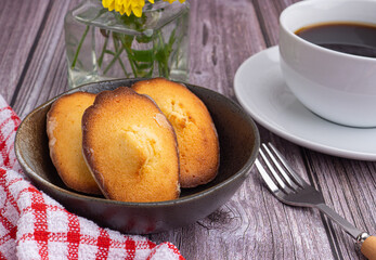 Madeleine homemade traditional French small cookies on black a dish with a cloth and a cup of coffee on a wooden background. Lemon glazed madeleines. Seashell sweet cakes