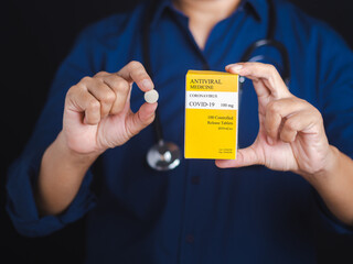 Hand of a doctor holding a pill and box of antiviral medicine COVID-19. Medicine for prevention and treatment from virus infection. Close-up photo. Concept of medical and the fight against the virus