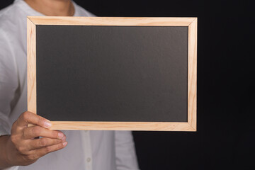 Hand of a man holding a small blackboard while standing in the studio with a black background. Space for text. Close-up photo