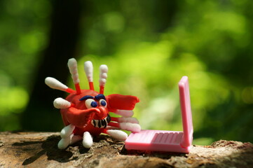 A close-up figure of a coronavirus made of plasticine. There is a toy laptop next to it. Business concept.