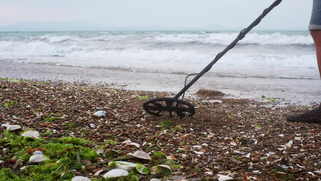 A man is looking for treasure with electronic metal detector on the beach and checking what he found. A luxury hunter on the sea beach in the morning