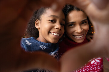 Crop close up of happy young African American mother and teen daughter make heart love hand gesture pose for selfie together. Smiling biracial mom and kid make self-portrait picture on holiday.