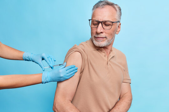 General practitioner vaccinates old male model gives injection against coronavirus. Bearded mature man cares about health gets vaccine to protecrt himself from flu or covid 19. Time to vaccinate