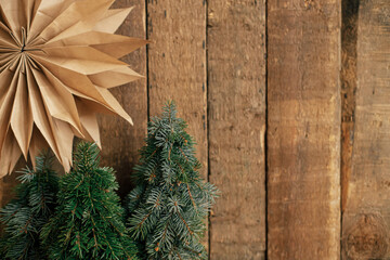 Merry Christmas! Stylish christmas paper star and little pine trees on rustic old wooden background. Space for text. Holiday advent. Season's greeting. Atmospheric moment. Handmade decor
