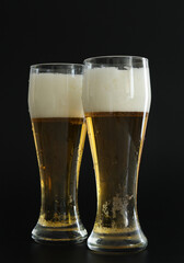 Two frosty glasses of cold golden beer with bubbles on the black background. Drinking alcohol on party, holidays, Oktoberfest or St. Patrick's Day.