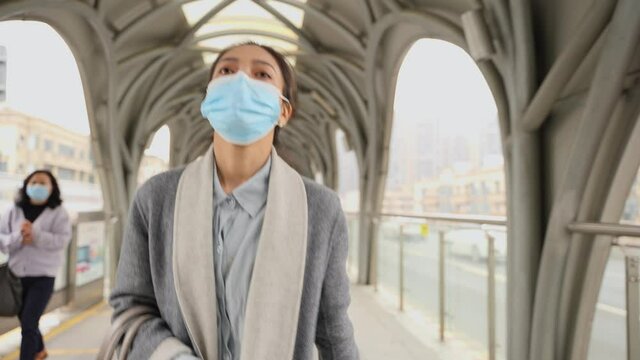 Asian businesswoman wearing mask looking at mobile phone walking at street bus stop