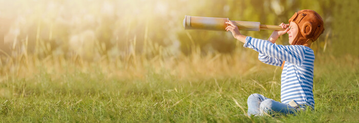 Little boy plays outdoors.
Cheerful and happy child stands and looks through the spyglass on the background of the forest - obrazy, fototapety, plakaty