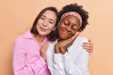 Photo of mixed race young women embrace and look gently at camera have friendly relationships...