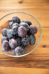 plums in a glass bowl on a wooden background. 