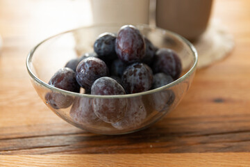 plums in a glass bowl on a wooden background. 