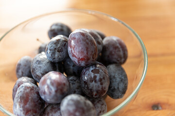 plums in a glass bowl on a wooden background. 