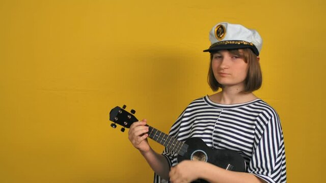 Young blonde girl plays ukulele guitar in the studio on the yellow background