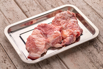 fresh raw pork neck meat fillet in stainless steel tray on old white wood texture background, ingredient for chop steak