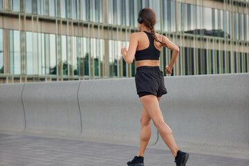 Outdoor shot of active slim woman has jog exercises being physically active covers long distance wants to come first at finish dressed in sportswear has morning workout. Back view of female jogger