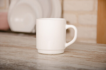 a white cup stands on a wooden table against a background of blurred plates with space for a logo or advertisement