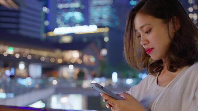 pretty young asian woman using phone in the urban city street at night