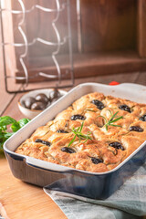 Traditional Italian Focaccia with black olives, herbs and oil on wooden table