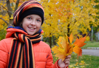 pretty girl in an orange jacket, beret and scarf holds bouquet of yellow maple leaves. Teenage girl...