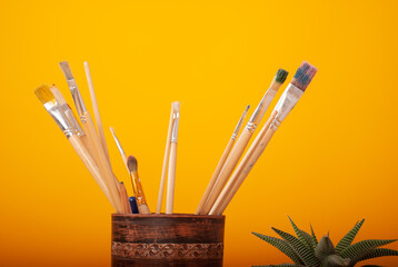 artistic brushes on a yellow background on a wooden table with paints and a palette with space for...