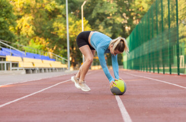 Obraz premium Athletic woman exercising in dynamics on medicine balls at the stadium
