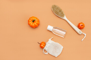 Autumn beauty season still life on a beige background. Small pumpkins, a body brush, liquid in a bottle on a beige background. Top view. Flatly.
