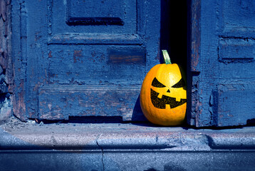 Halloween background. A naughty pumpkin peeking out from behind an old abandoned door.