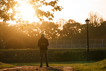 Senior man runner in autumn park using smartphone during sunset 