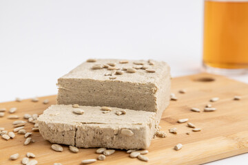 A piece of sunflower halva and sunflower seeds on a wooden cutting board next to a green towel