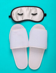 Sleeping mask with eyelashes and slippers on a blue background. Top view
