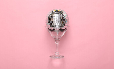 Minimal party layout. Cocktail glass with false eyelashes, disco ball on a pink pastel background. Top view