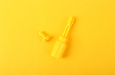 Yellow plastic screwdriver with screw on yellow background