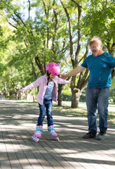 dad teaches daughter to roller skate.