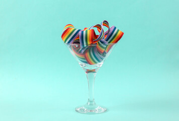 Rainbow lgbt ribbon in a cocktail glass on a turquoise background. Lgbt community, party